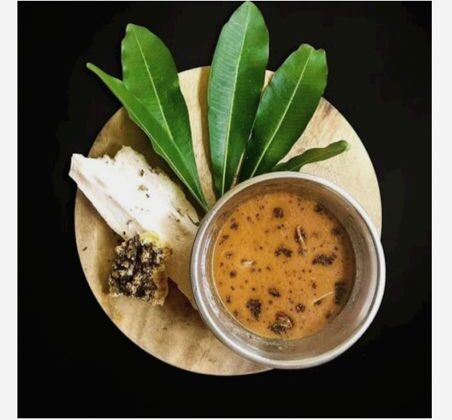 A bowl of dark Aati Kashaya decoction beside medicinal bark and fresh mango leaves for Aati Amavasya