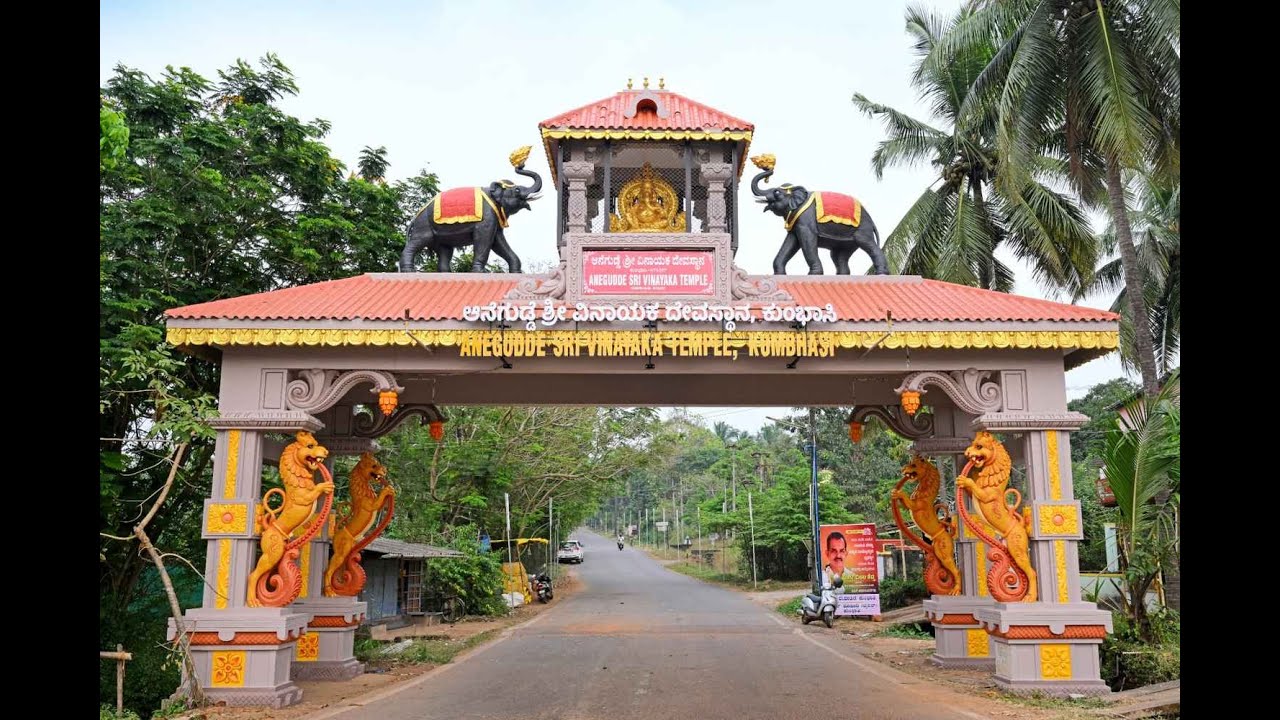 The decorated road gateway to the Anegudde Sri Vinayaka temple at Kumbashi, with carved elephants, rampant lions and a golden Ganesha shrine on top, framed by coconut palms