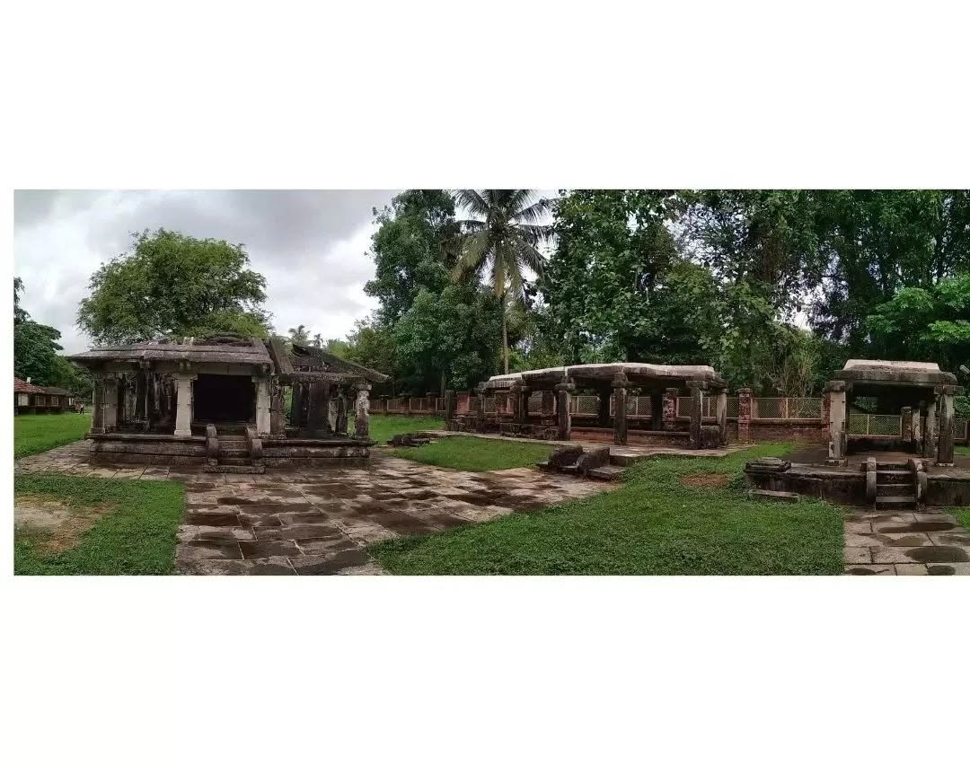 A wide view of the Barkur monument complex with a shrine on the left and rows of open stone pavilions across a grassy clearing