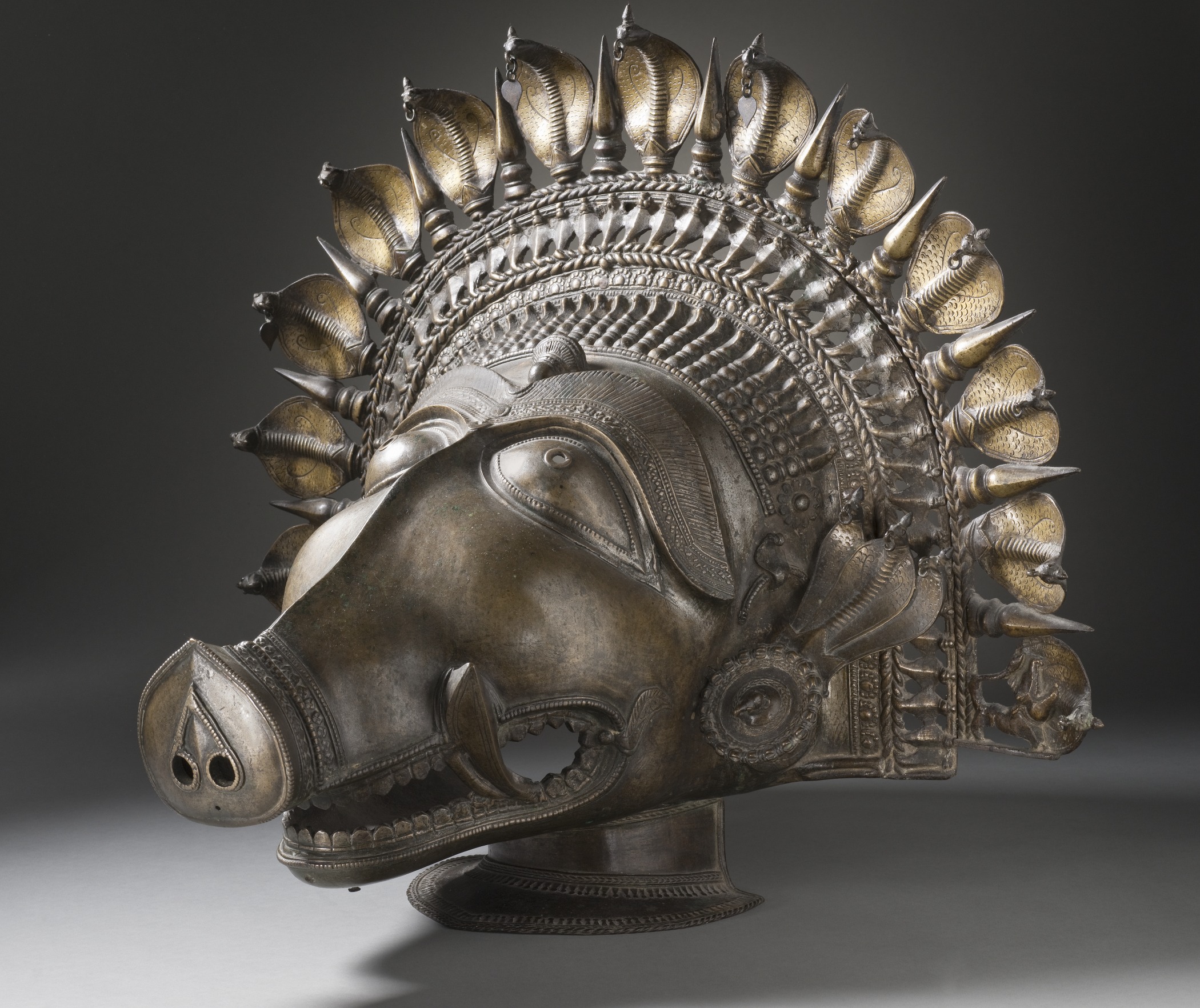 An antique cast-bronze dancer's headpiece in the form of the boar-faced spirit deity Panjurli, ringed by a halo of cobra hoods and spikes