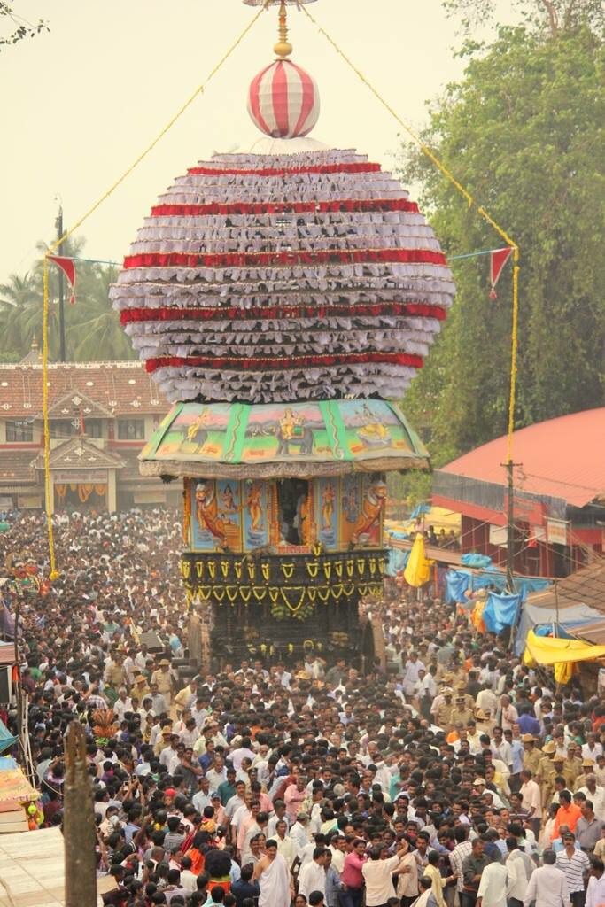 A towering temple chariot decorated with red and white cloth tiers being pulled through a packed crowd at a Kundapura Rathotsava