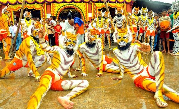 A group of Huli Vesha dancers pose in formation in front of a garlanded temple as a crowd watches