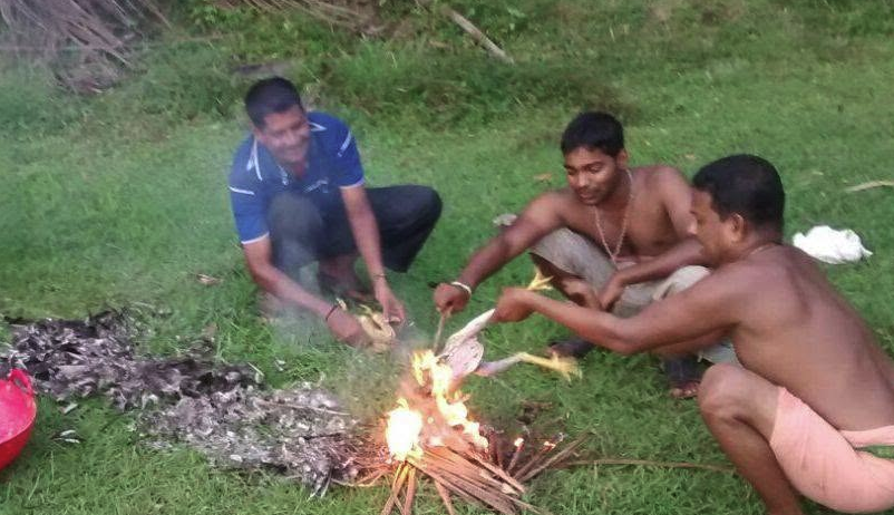 Men cooking the ritual offerings over an open wood fire on the grass during a Jakni family gathering