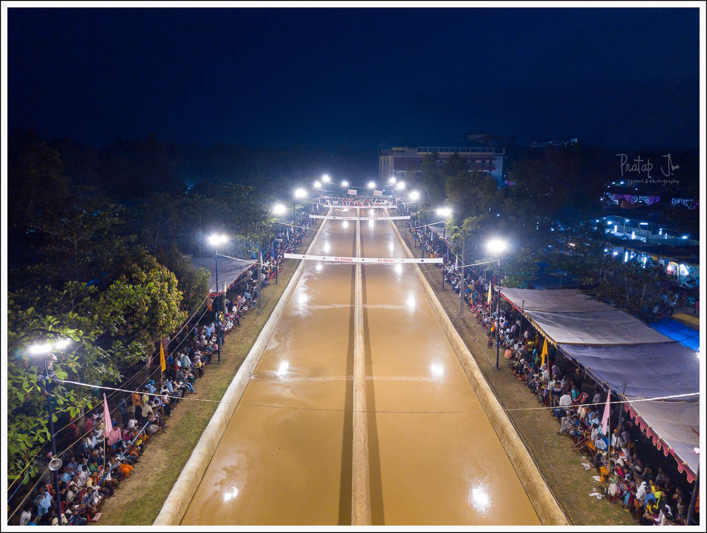 An aerial night view of the twin-lane water-filled Kambala track lit by floodlights, lined with thousands of spectators