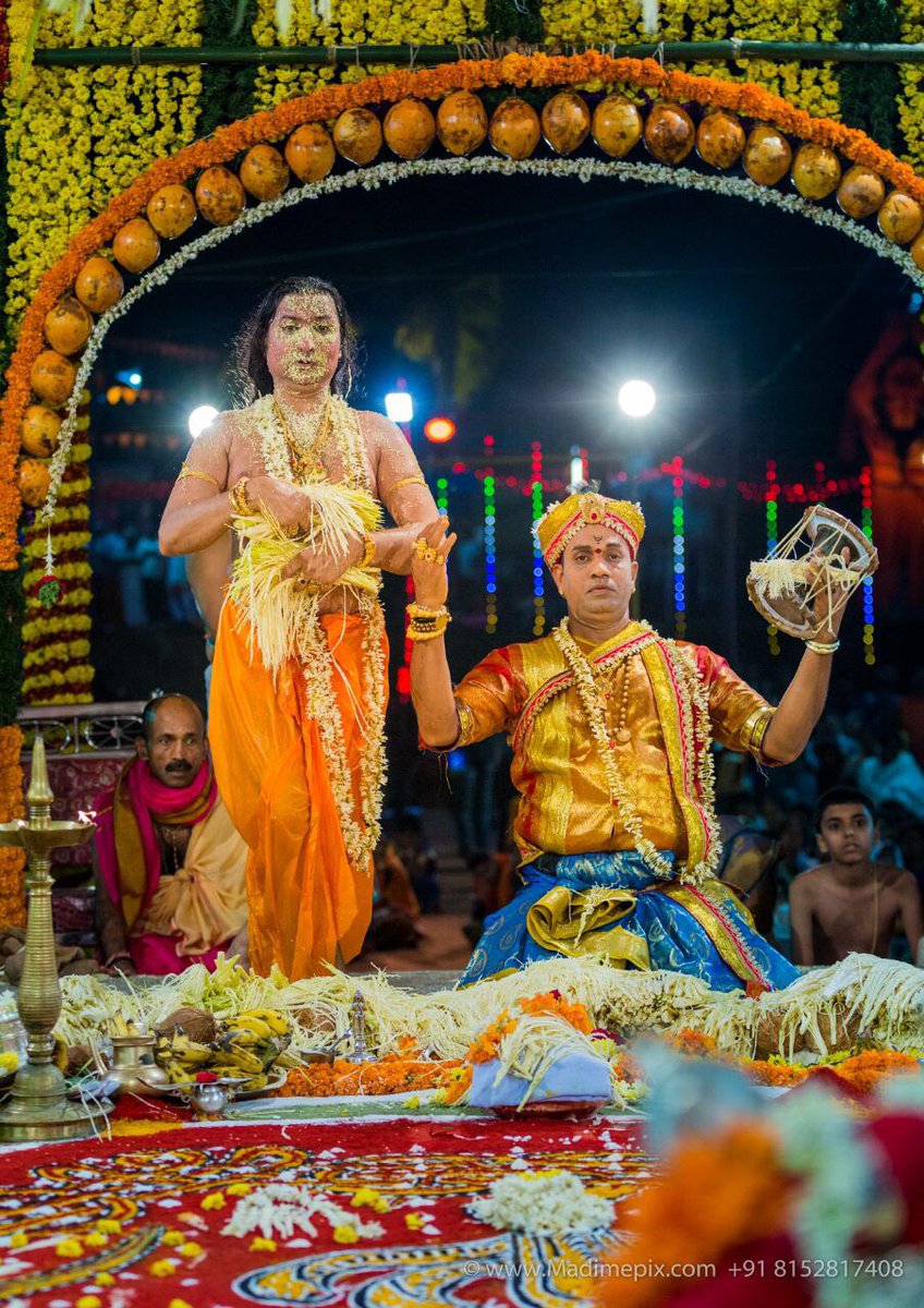 A Naga Patri in serpent-hooded crown and red costume in a state of divine inspiration, holding ritual implements before the gathered devotees