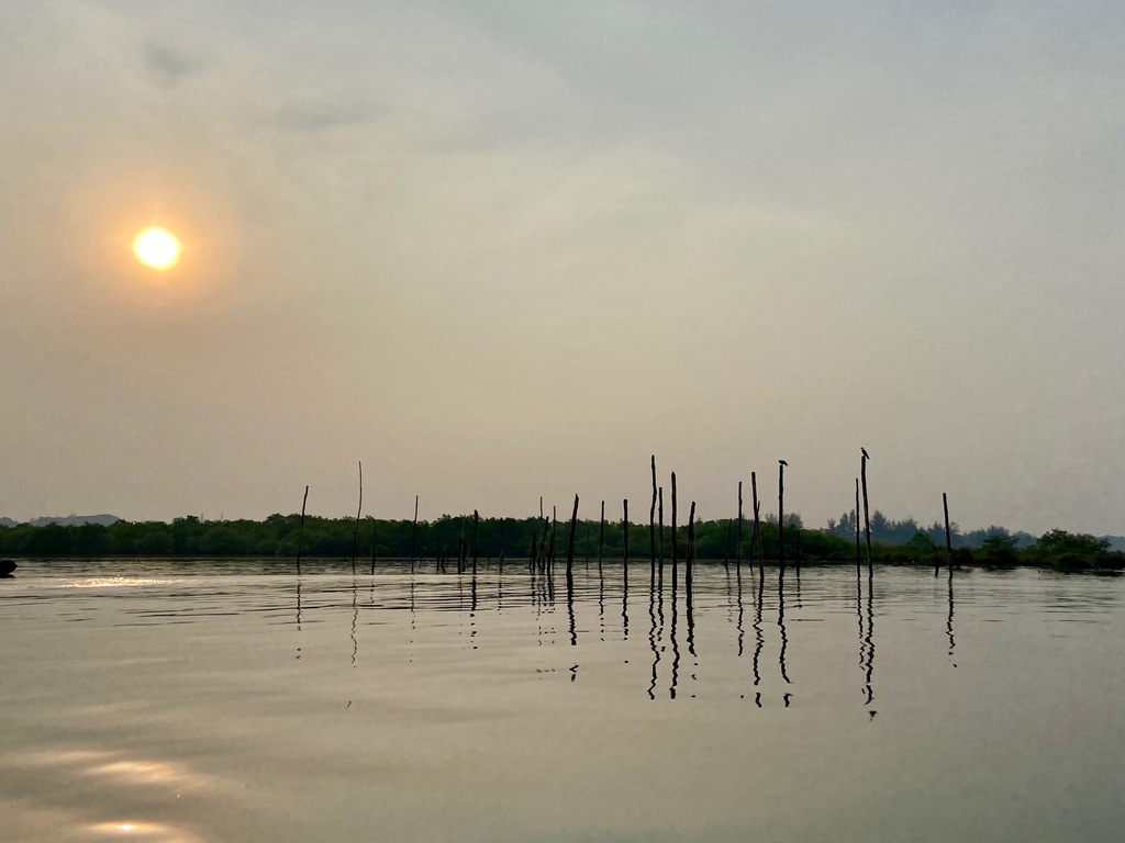 The hazy sun low over the estuary with fishing stakes mirrored in still water