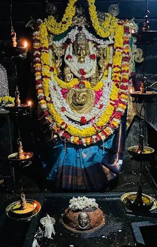 The garlanded deity of Sri Brahmi Durgaparameshwari at Kamalashile, framed by a kirtimukha and surrounded by oil lamps