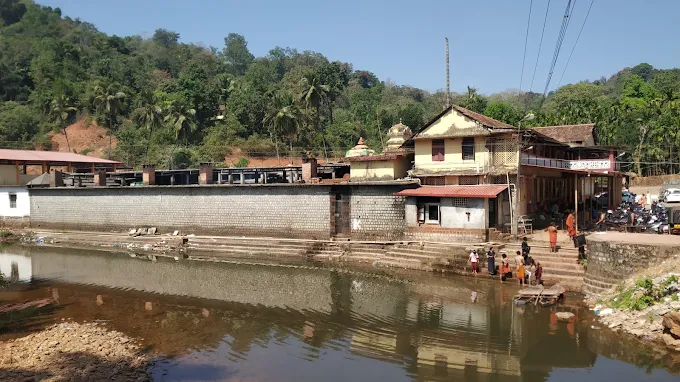 The Kamalashile temple complex seen across the calm waters of the Kubja river, with stone ghats and green hills behind