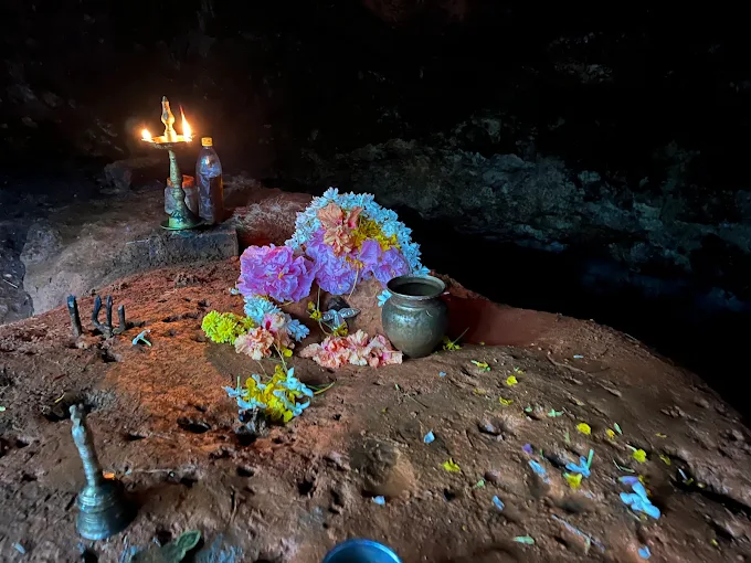 An interior shrine inside the cave with fresh flowers, a brass pot and an oil lamp on the bare rock